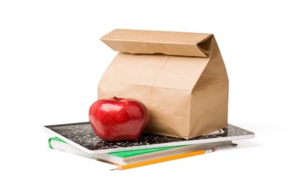 Brown paper lunch bag and a red apple sitting on top of textbooks against white background.